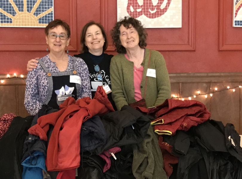 three women standing behind clothing donations